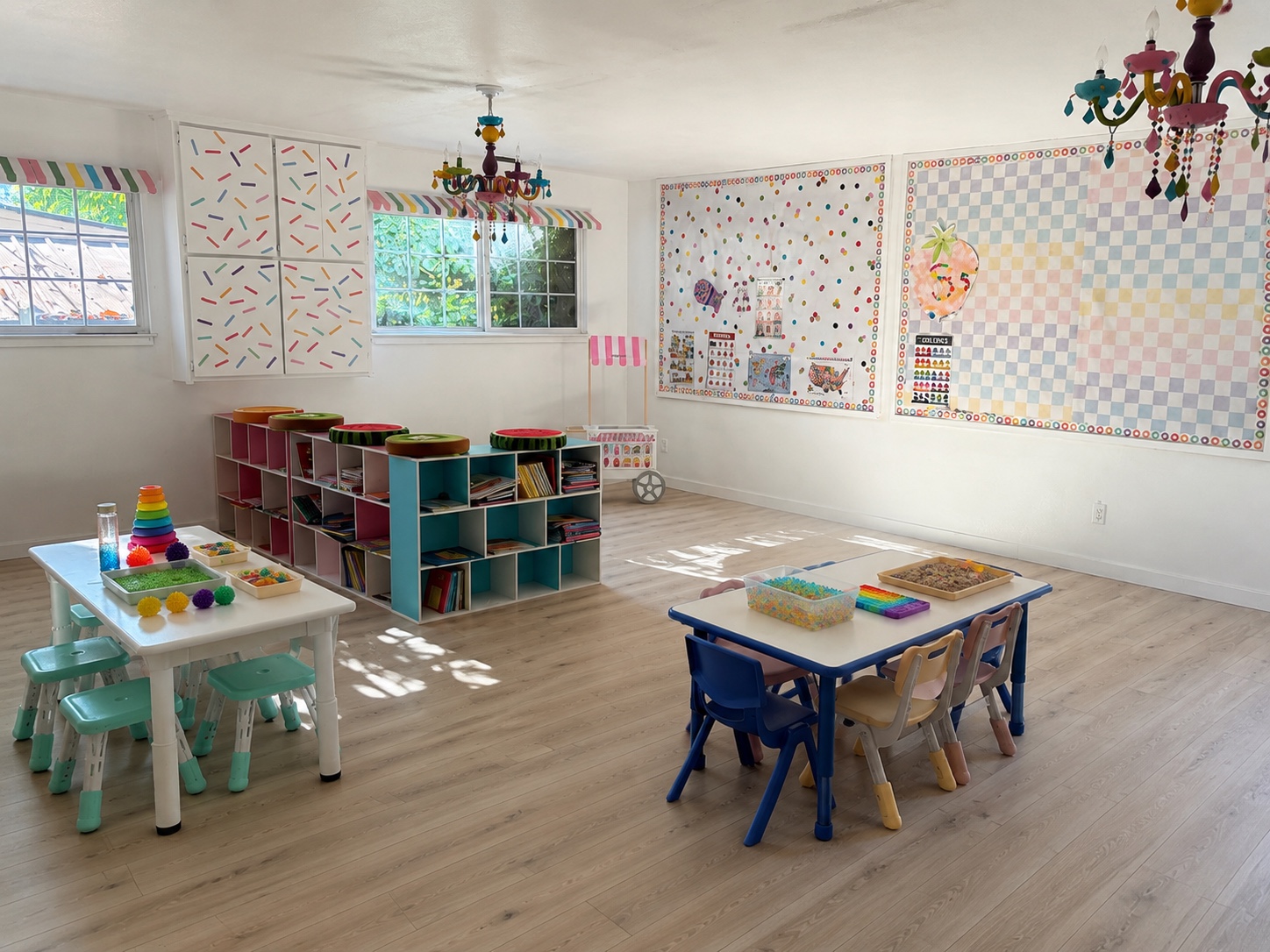 Bright activity room with sensory tables, book cubbies and colorful chandeliers